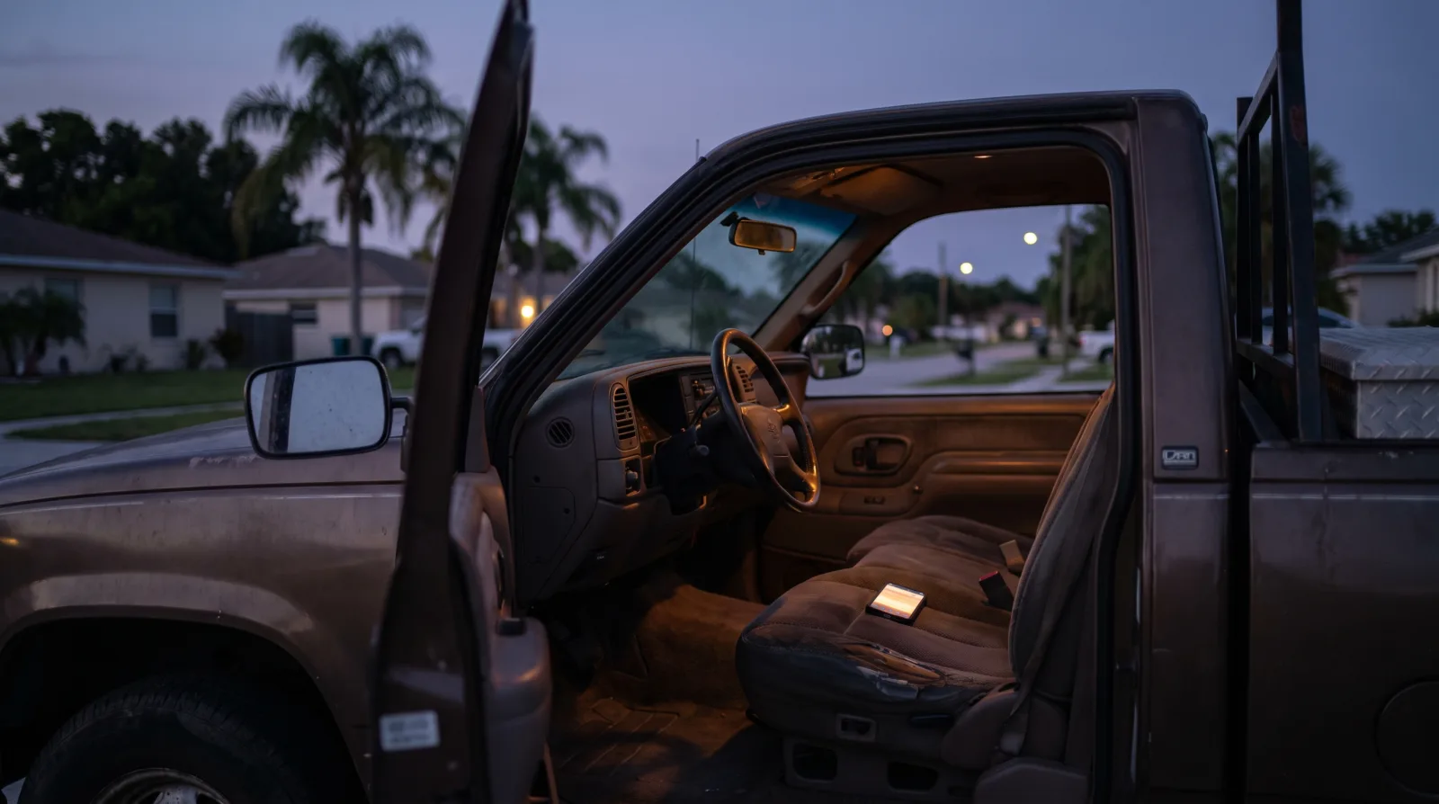 An open work truck door at dusk with a phone lit up on the driver's seat
